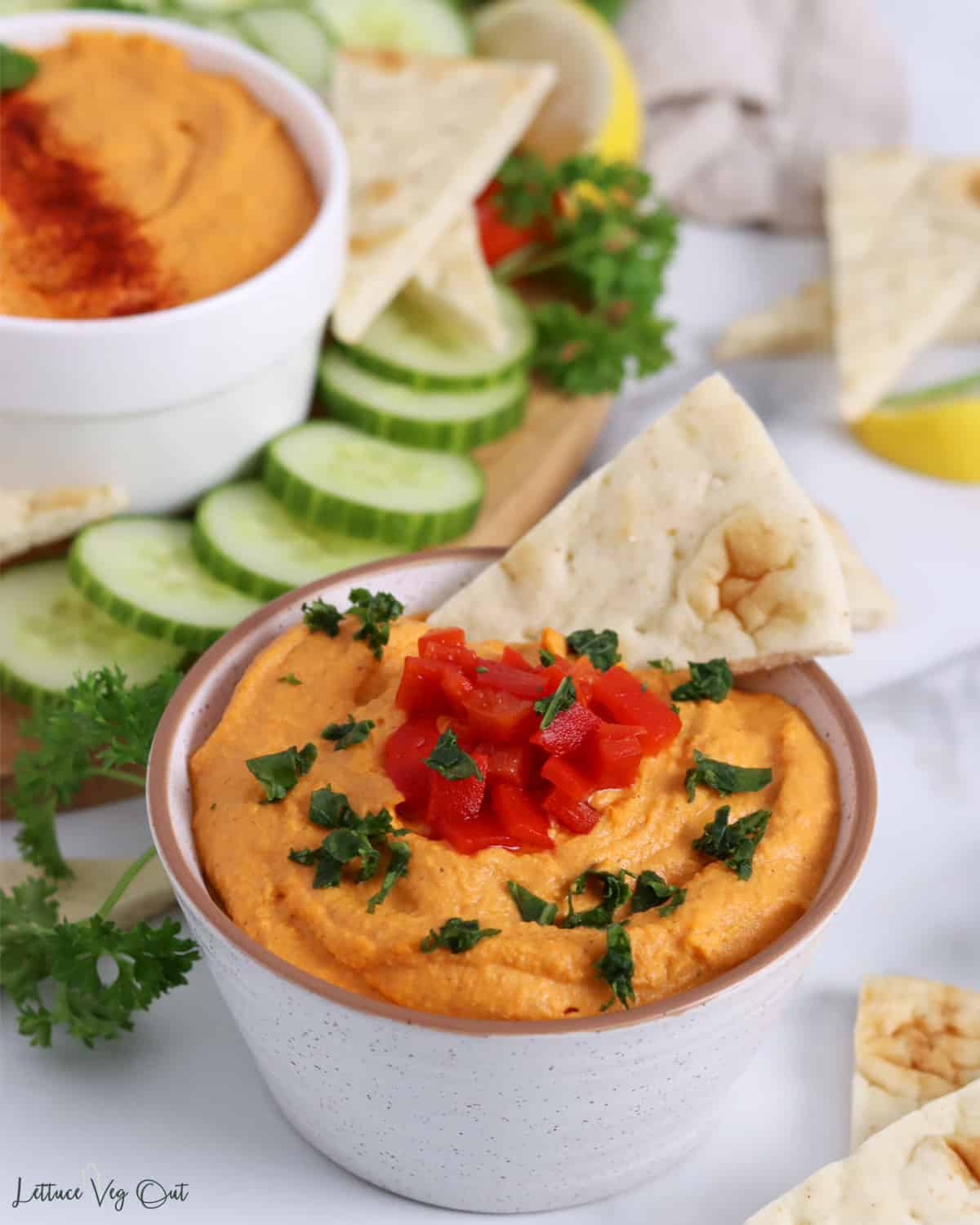Bowl of roasted red pepper hummus with pita bread dipped in it.