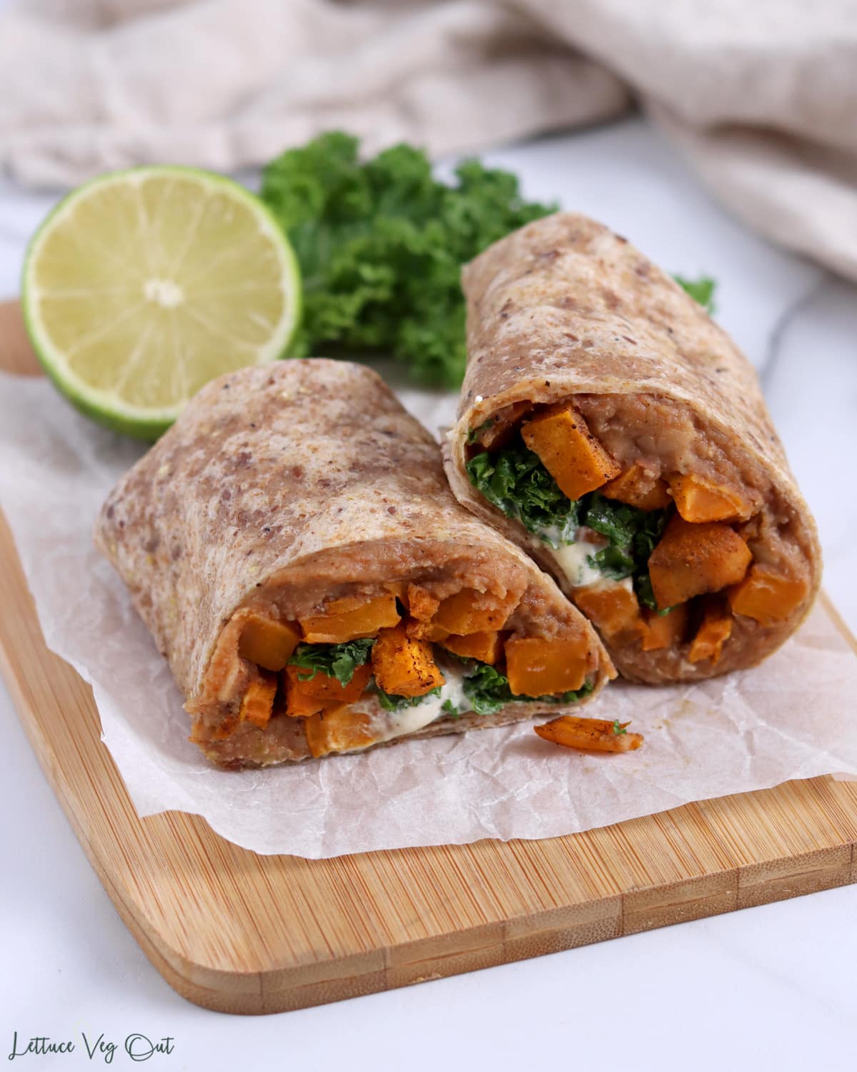 Close up of a burrito that is cut in half showing a sweet potato, refried bean and kale filling.
