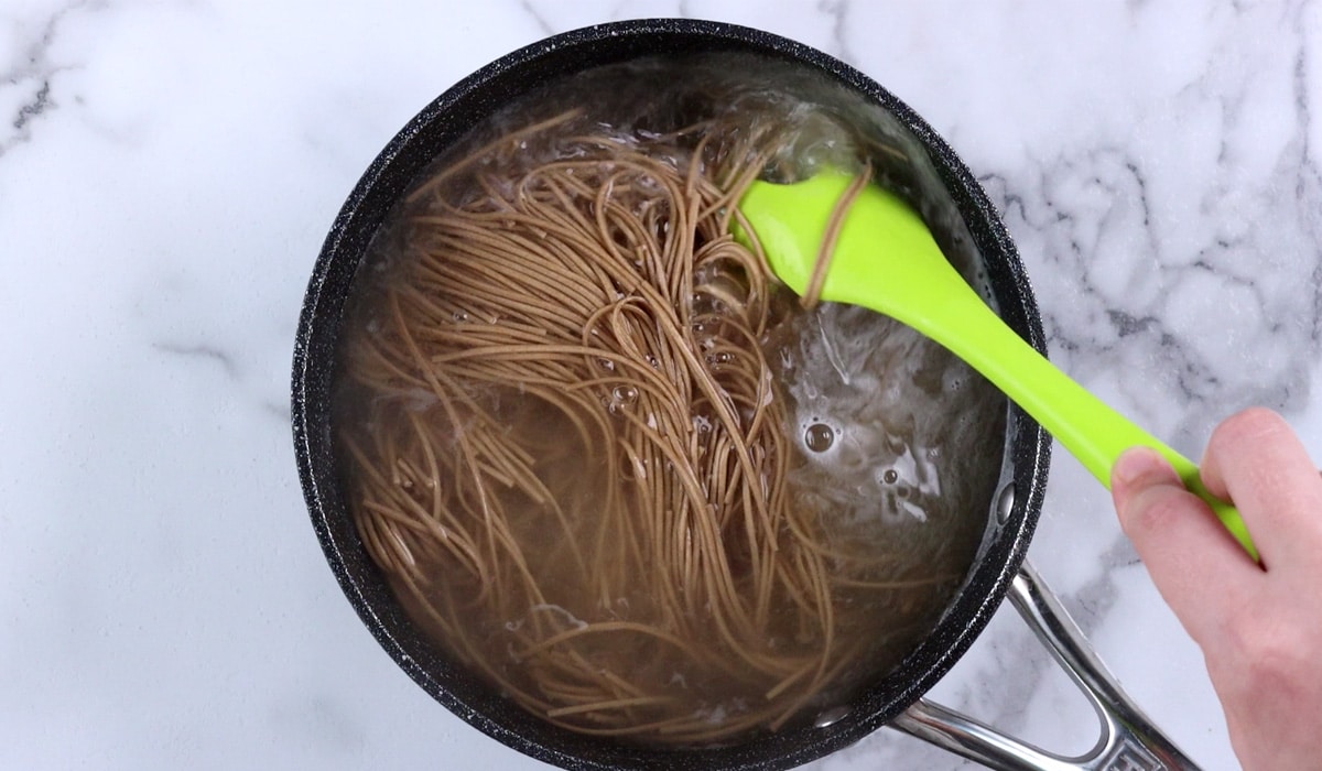 Stirring soba noodles in a pot of water.