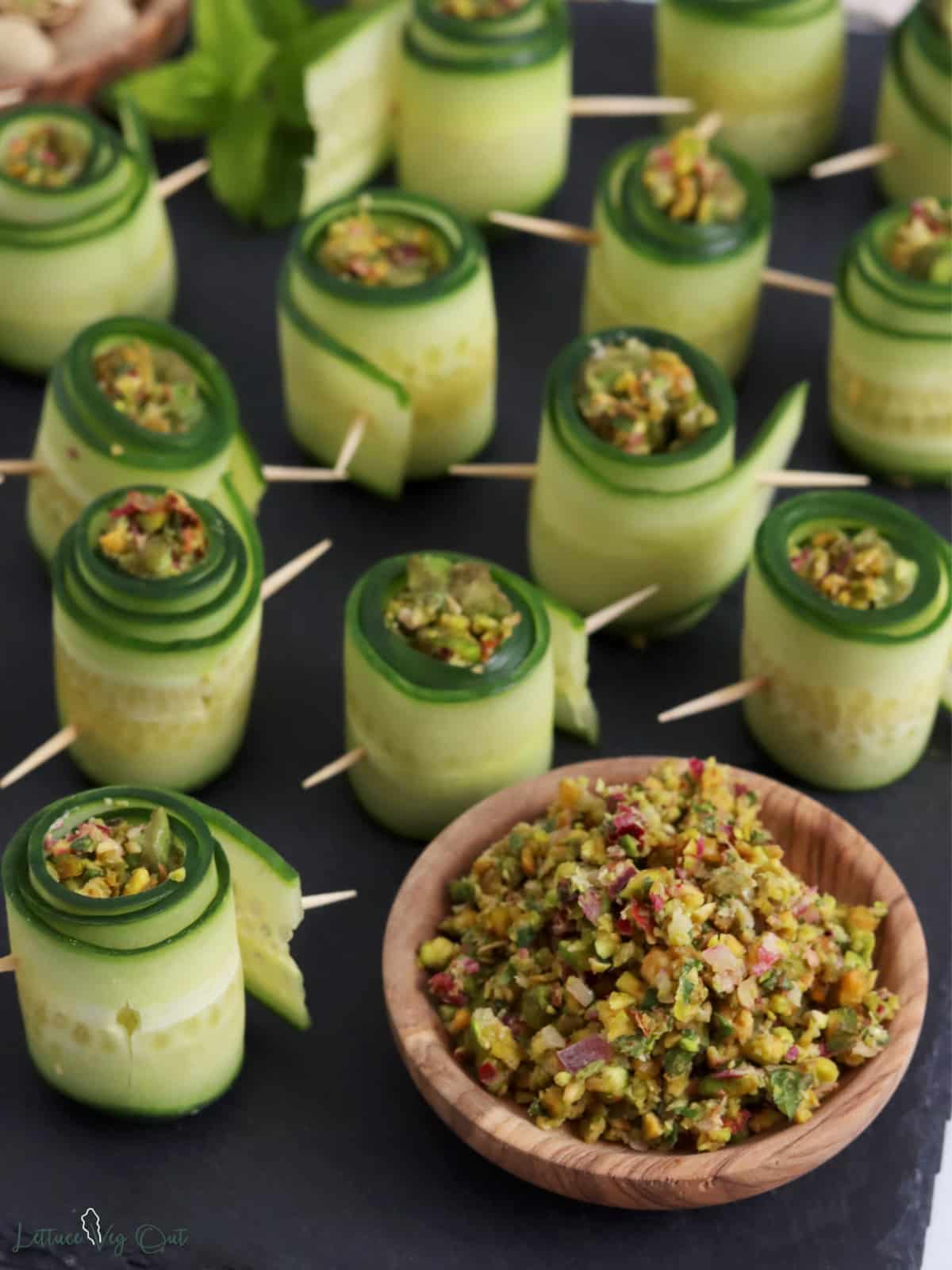 Small dish of ground pistachio filling in front of cucumber roll ups.