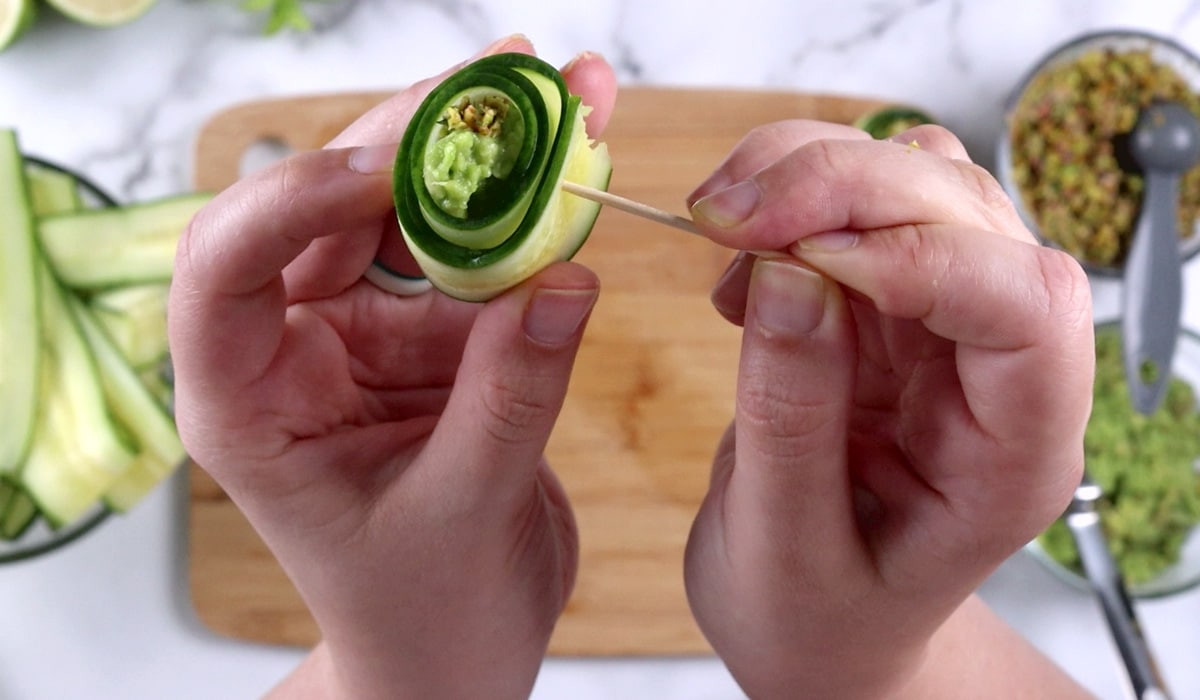 Poking a toothpick through a cucumber rollup.