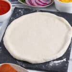 Close up of a rolled out pizza dough with pinched crust edge on slate board.