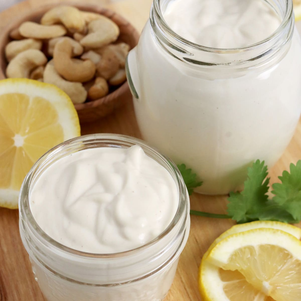 Close up of two small jars of creamy cashew mayonnaise with cashew and lemon garnish.