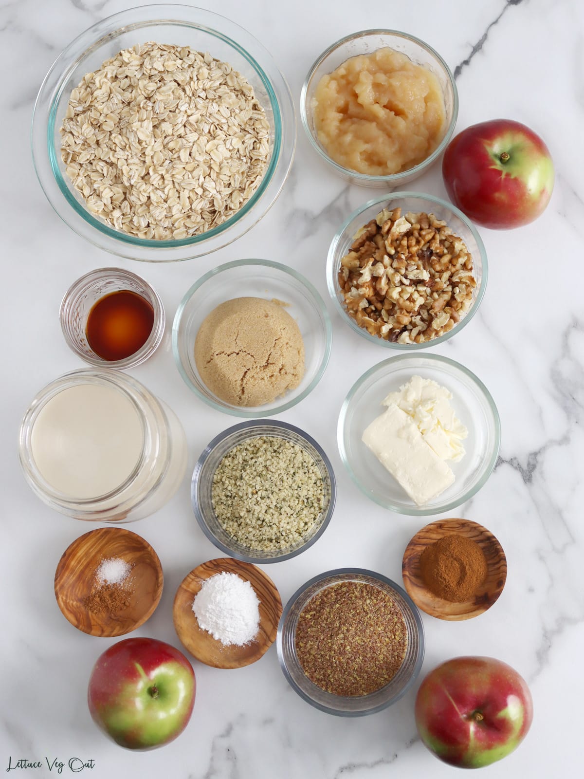 Arrangement of ingredients, in glass and wood dishes, for apple baked oatmeal.
