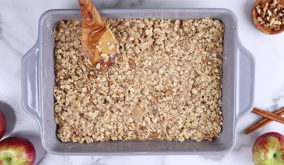 Spreading raw oatmeal mixture into ceramic baking dish with a large wood spoon.