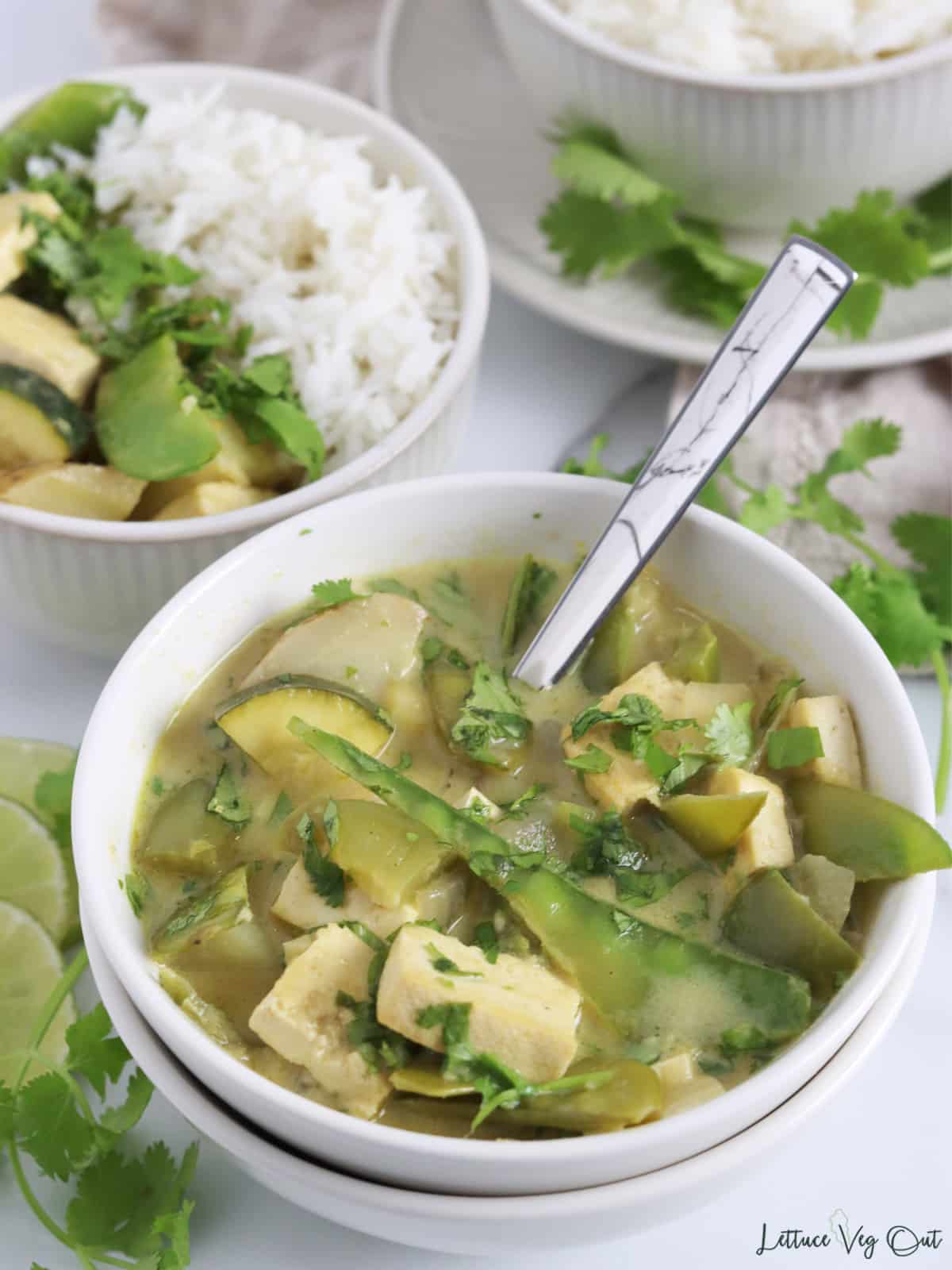Close up of a small bowl filled with tofu green curry with snow peas, zucchini, potato and cilantro garnish.