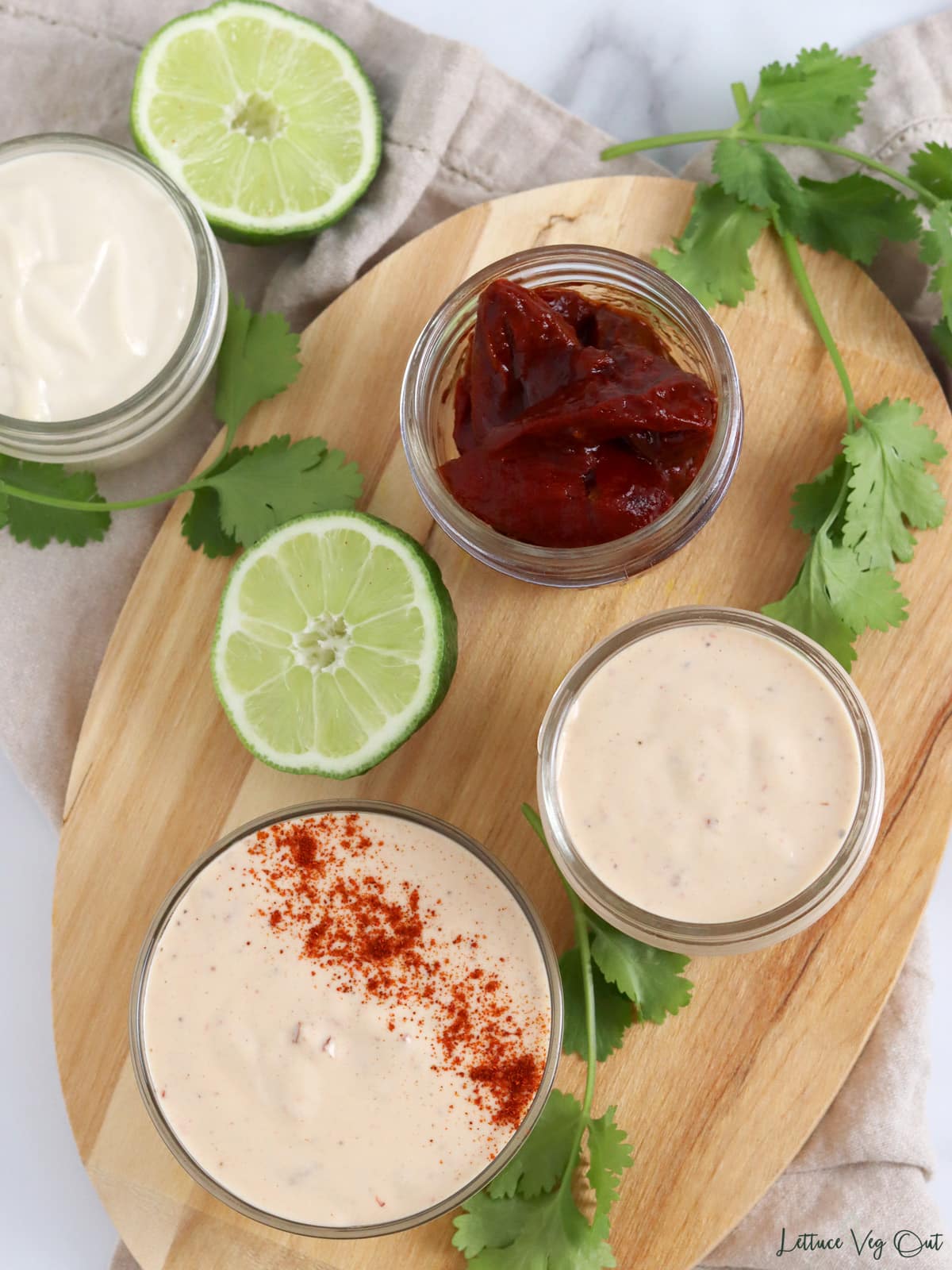 Two glass jars of chipotle mayo with third jar of chipotle peppers on wood board with lime and cilantro garnish.