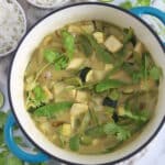 Close up of a large pot of tofu green curry with zucchini, snow peas and potato with cilantro garnish.