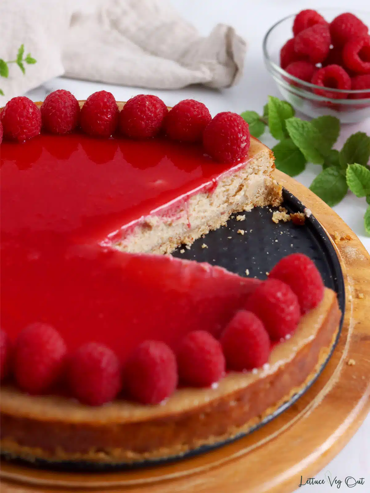 Cheesecake with raspberry sauce and fresh raspberry topping with slices cut out, showing texture of cheesecake.
