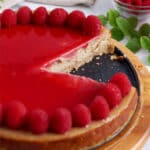 Close up of a raspberry cheesecake with slices removed to show texture, topped with fresh raspberries and raspberry sauce.