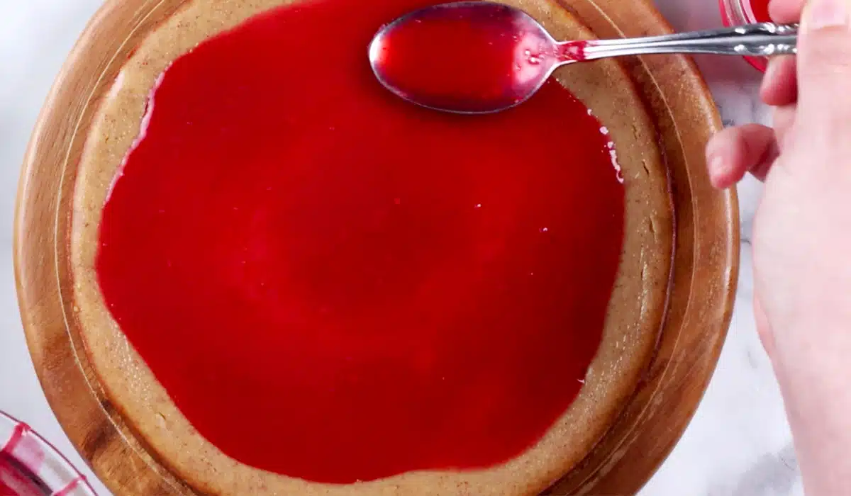 Spreading raspberry sauce onto top of cheesecake.