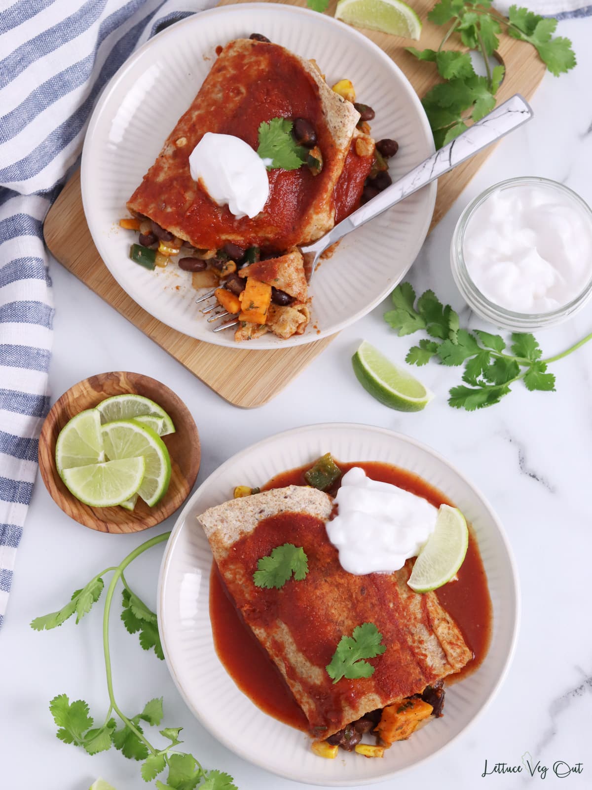 Two plates of black bean sweet potato enchiladas with red sauce, topped with sour cream and lime garnish.