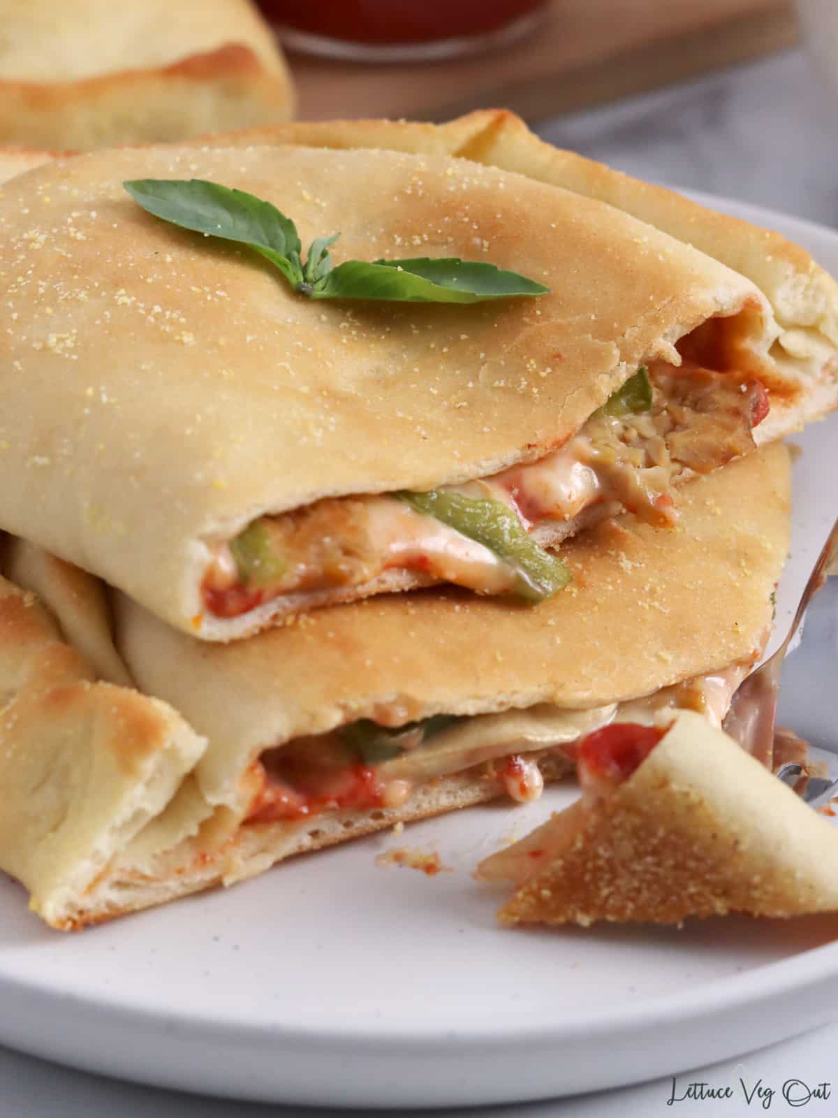 Stack of two calzones halves on a plate with melted cheese, green pepper and tempeh filling visible.