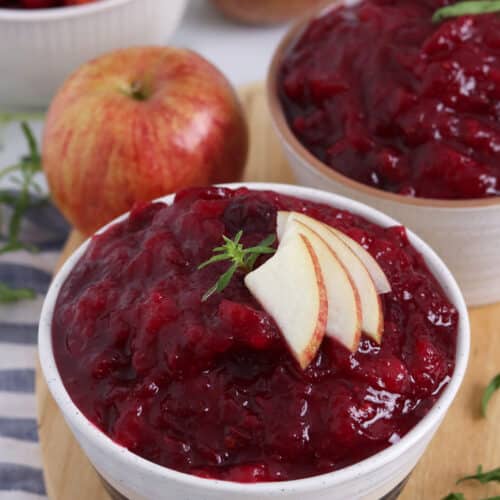 Close up of two bowls filled with cranberry sauce, with an apple garnish.