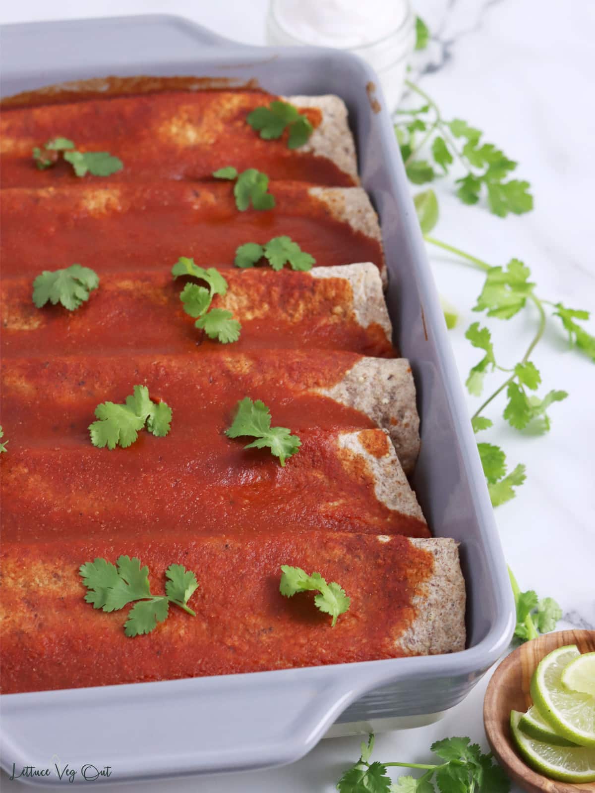 Casserole dish filled with baked enchiladas, topped with red sauce and cilantro garnish.