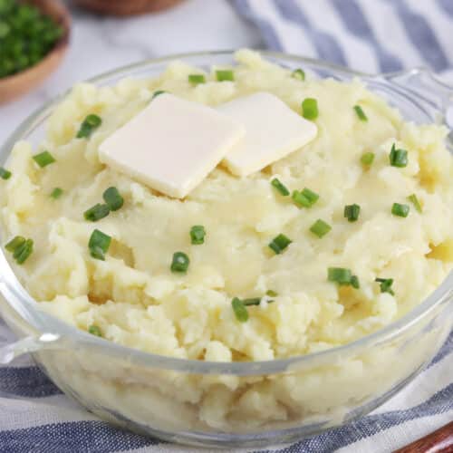 Close up of a glass bowl filled with vegan mashed potatoes topped with butter and chives.