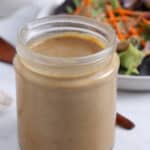 Close up of jar filled with creamy balsamic tahini dressing with blurred salad in back.