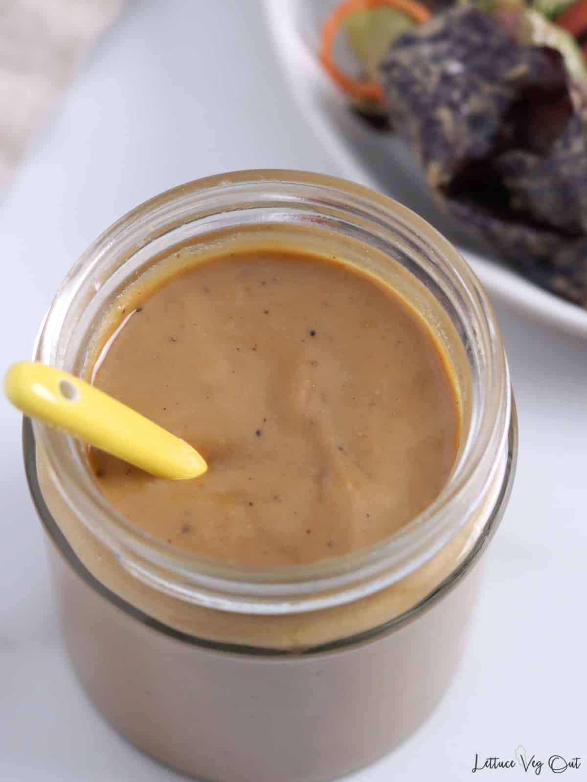 Top view of jar of balsamic tahini dressing with small yellow spoon in it.