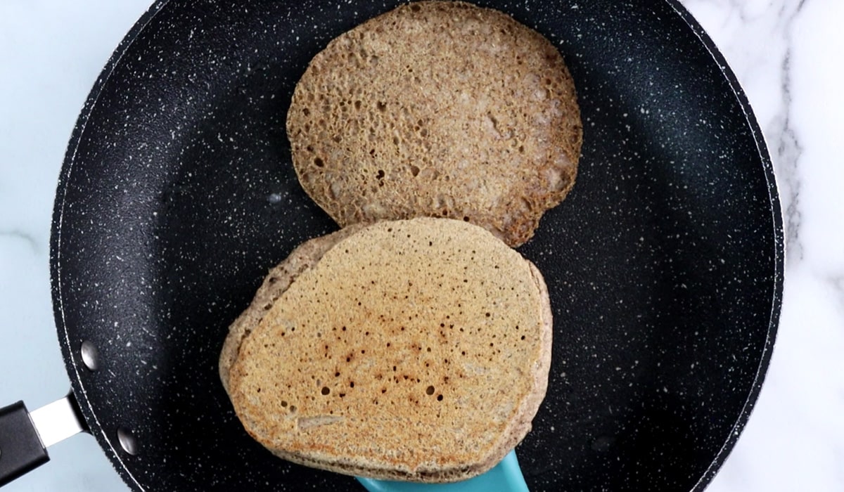 Spatula holding a cooked, lightly browned, buckwheat pancake over a pan with a second pancake in it.