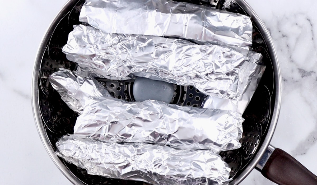 Tin foil wrapped seitan sausages in a pot.