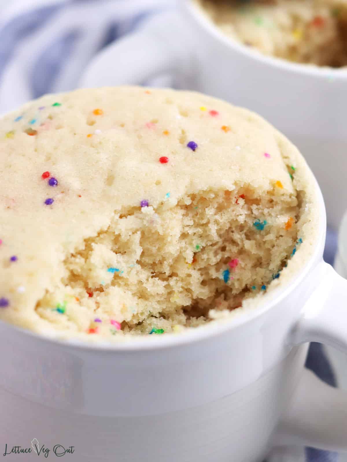 Close up of vanilla cake in a mug with a bite taken out to show inside texture.
