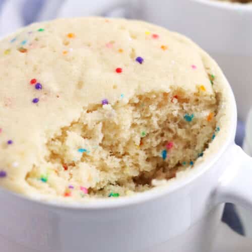Close up of a vanilla cake with sprinkles with a bite removed showing a fluffy, soft texture.