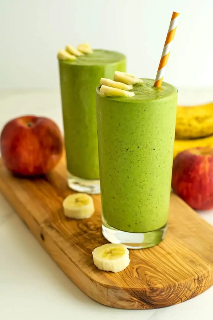 Two tall glasses of green smoothie with banana slices for garnish.
