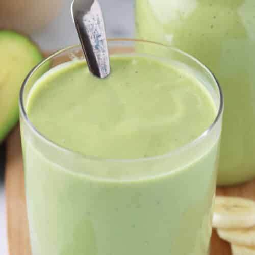Close up of glass filled with creamy avocado peanut butter banana smoothie with a spoon in the glass.