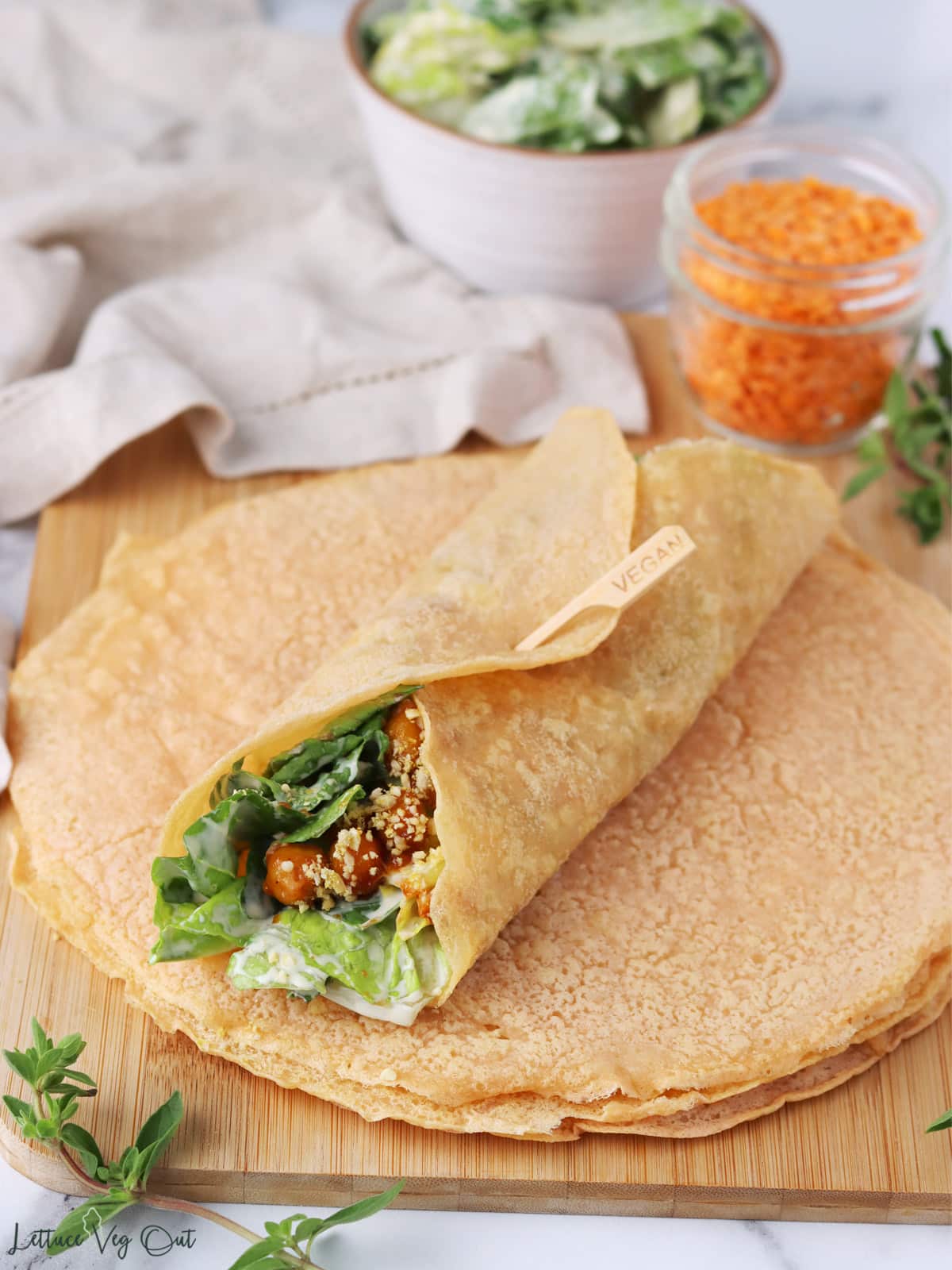 Stack of red lentil tortillas with one tortilla wrapped around salad on top.