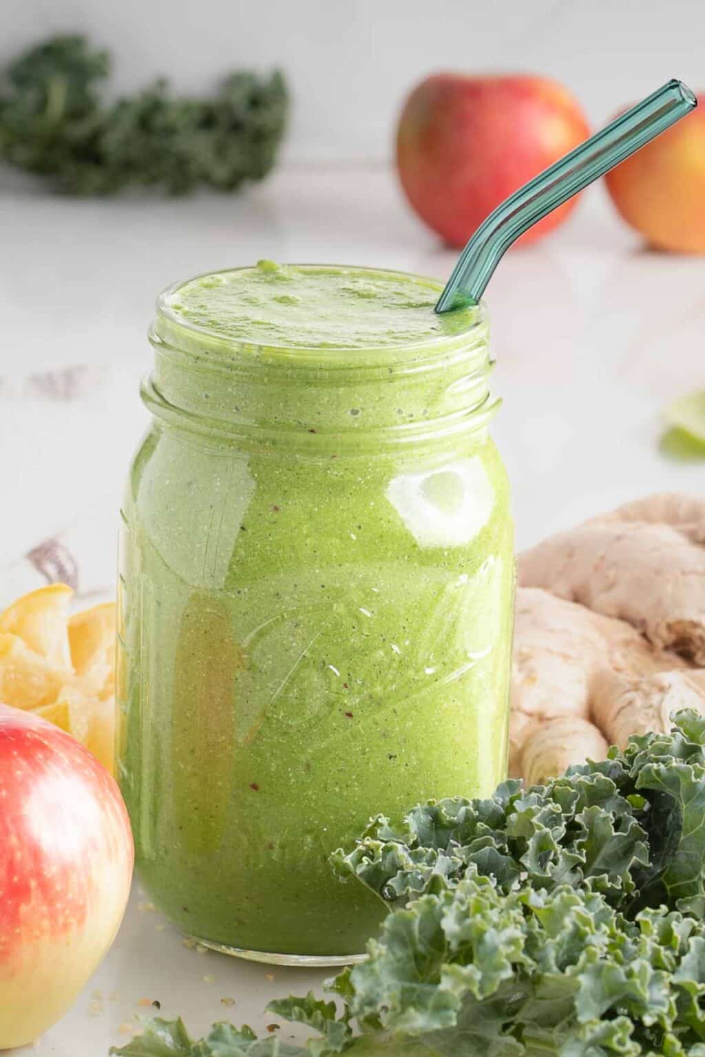 Mason jar with bright green smoothie surrounded by apple, kale, lemon and ginger.