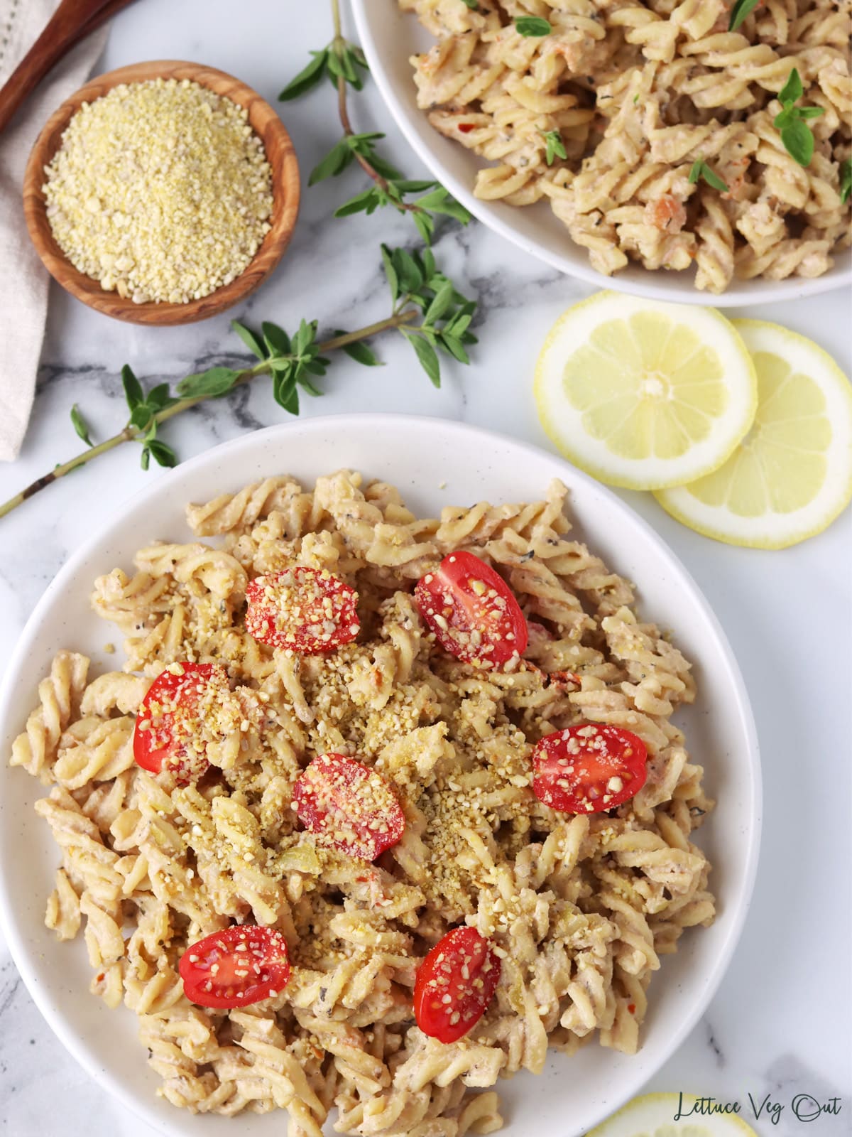 Plate of rotini pasta with creamy tahini sauce, topped with cherry tomatoes and vegan parmesan cheese.