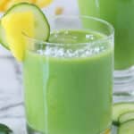 Close up of a glass of spinach pineapple smoothie garnished with pineapple and cucumber on the edge of the glass.