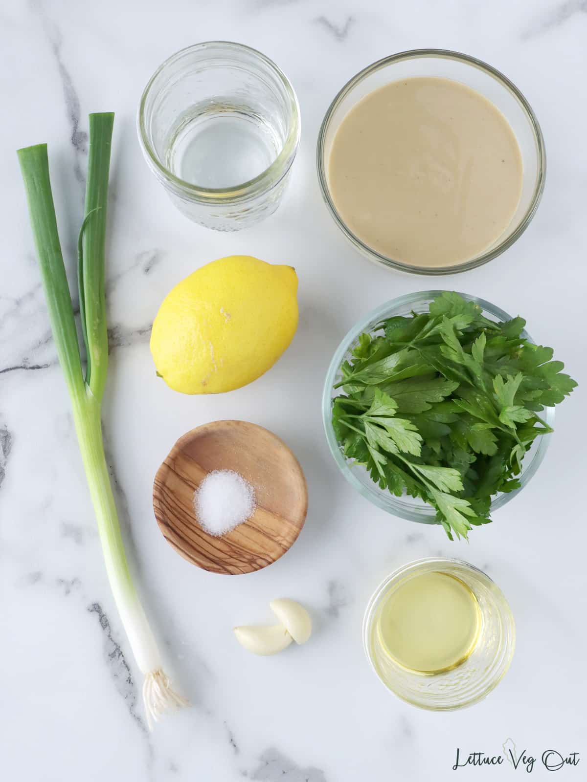 Ingredients for lemon tahini dressing in small dishes, on a marble board.