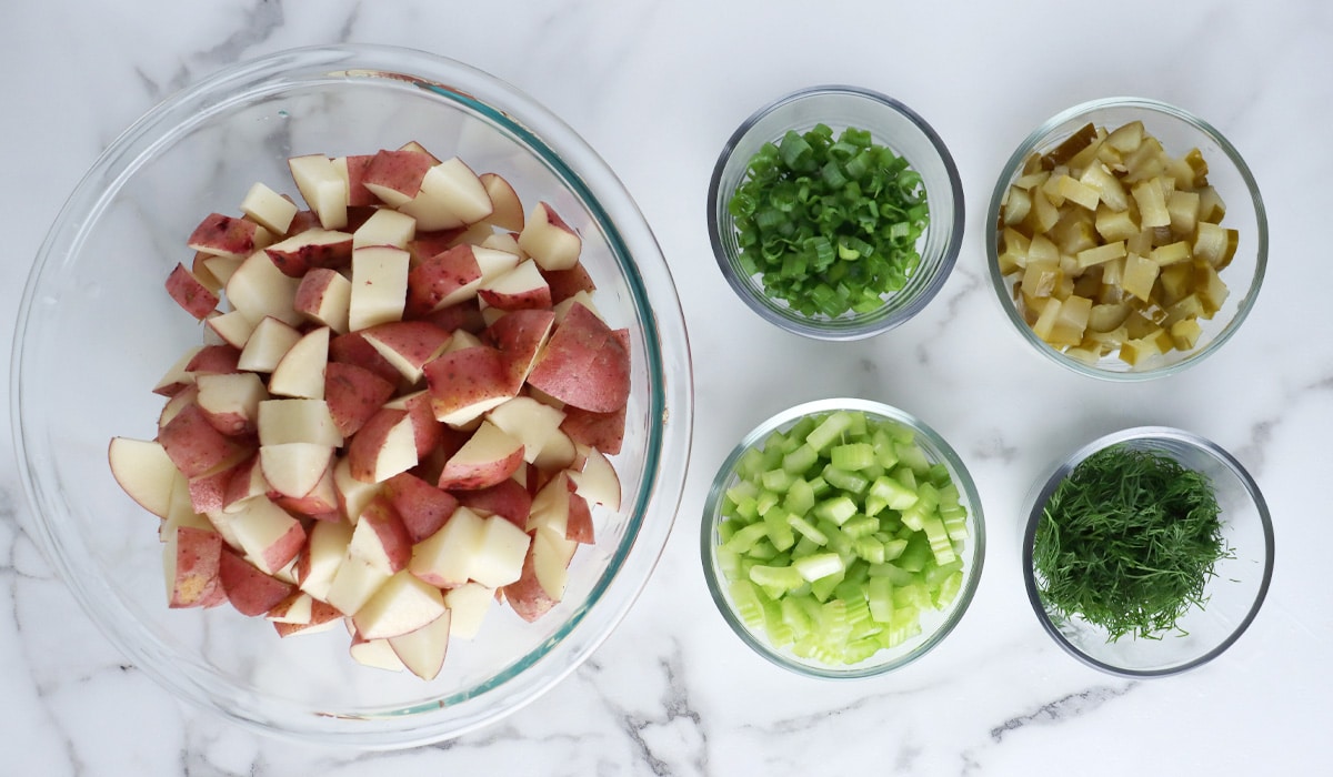 Glass dishes with chopped ingredients (red potatoes, green onion, dill pickles, celery, dill).