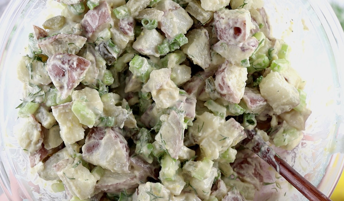Close up of a glass serving bowl filled with creamy potato dill salad.