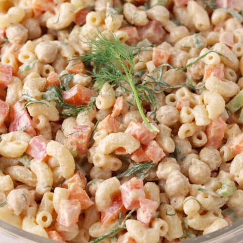 Close up of buffalo pasta salad with chickpeas, carrot, red pepper and celery in creamy dressing and fresh dill garnish.
