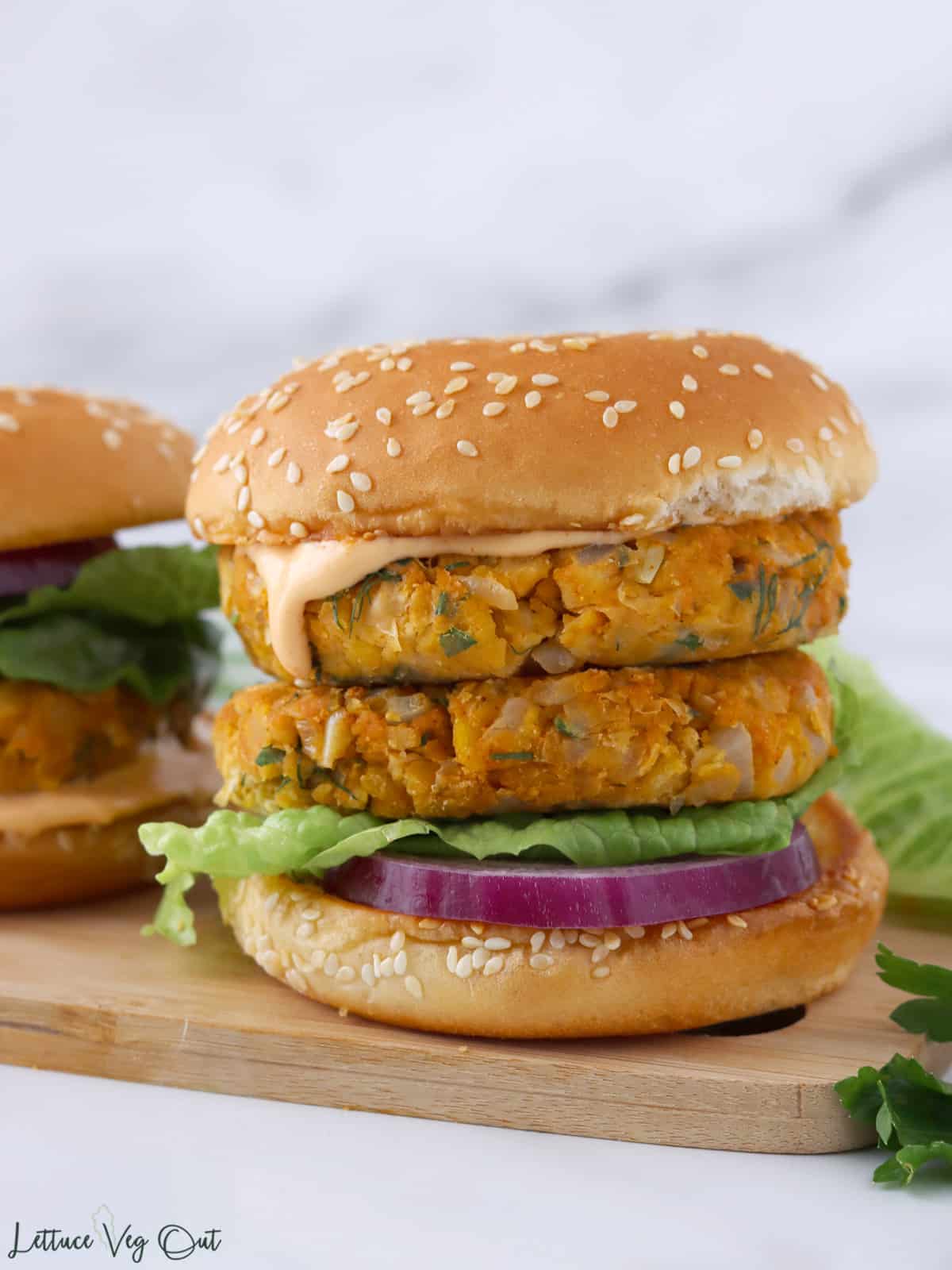 A double stacked chickpea patty burger with a fluffy bun, sriracha mayo, red onion and lettuce.