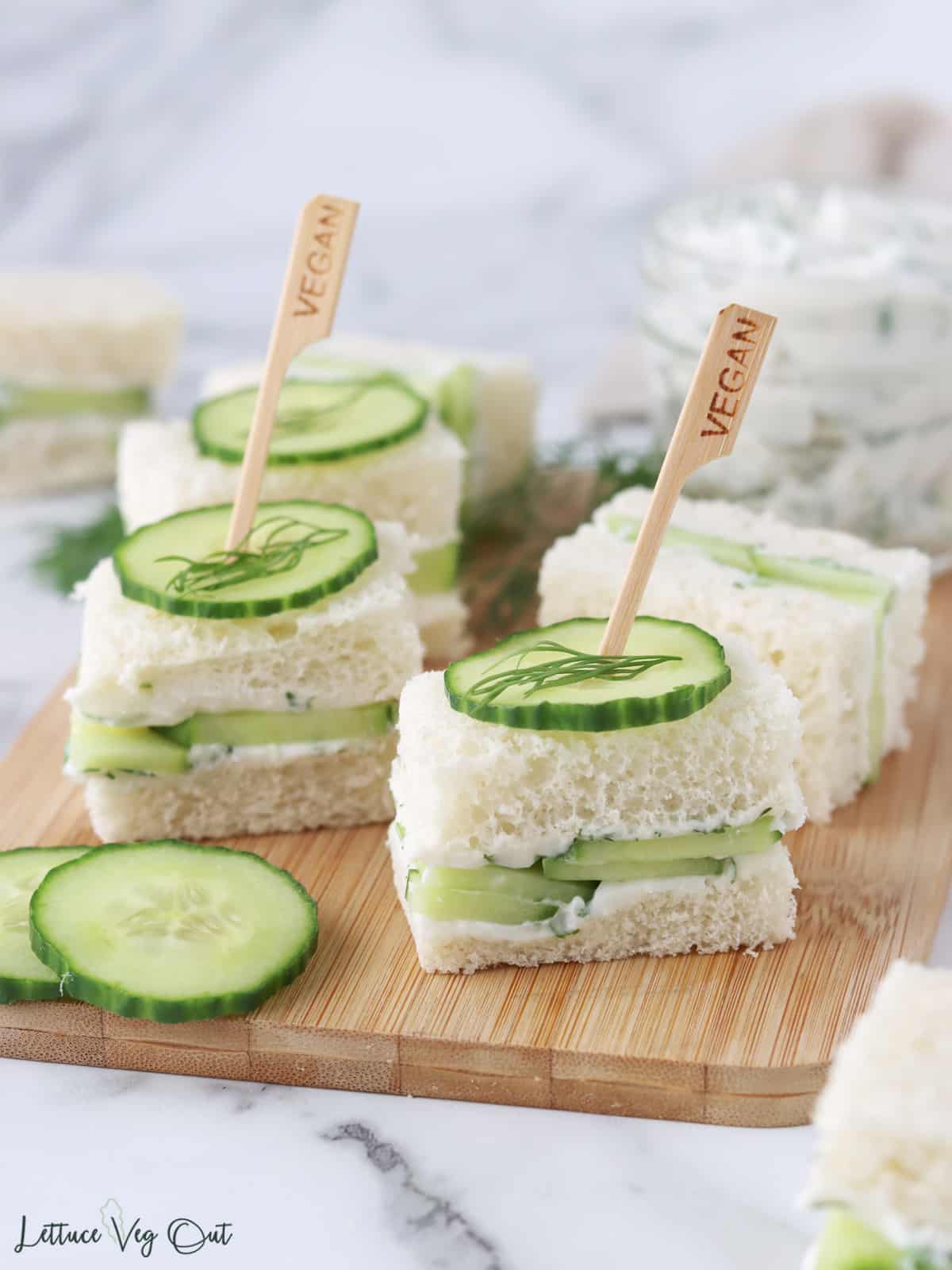 Close up of vegan cucumber sandwiches with cucumber and dill garnish on top, skewered with a toothpick.