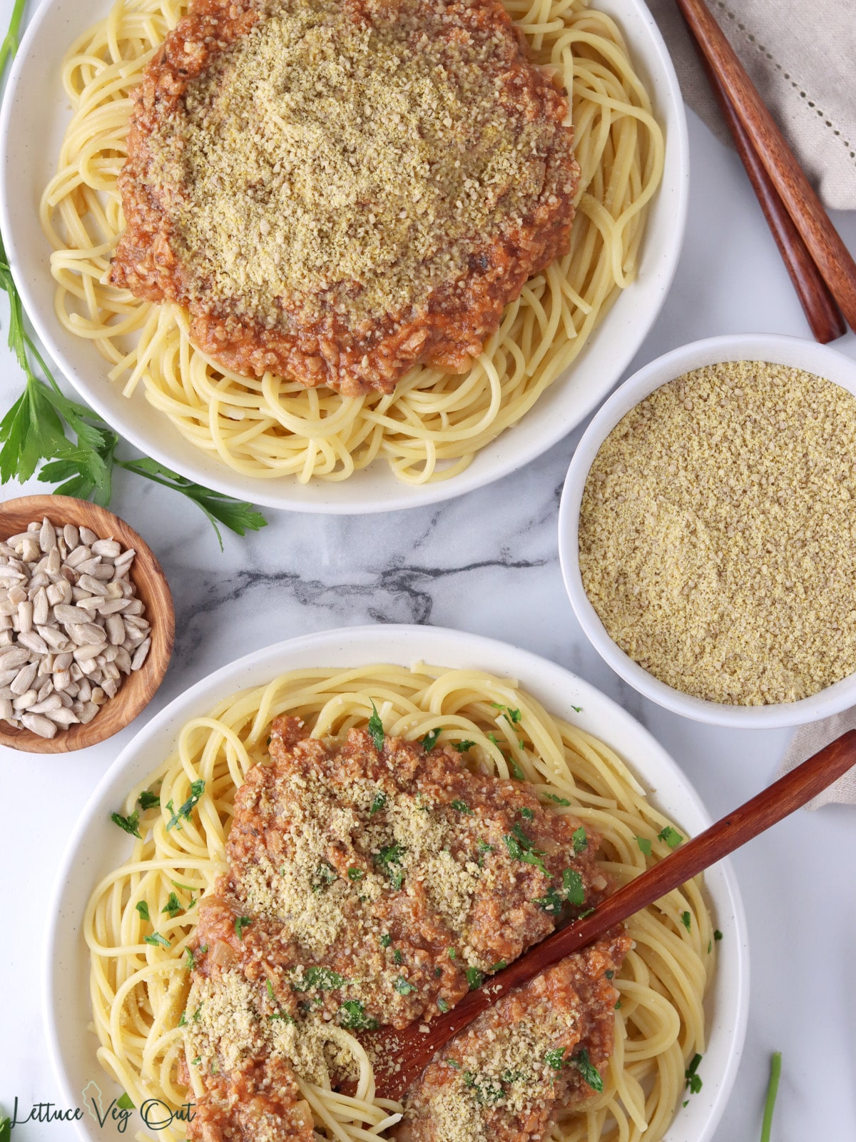 Two plates of spaghetti topped with tomato sauce and sunflower seed parmesan, next to dish of sunflower seeds and dish of sunflower parm.