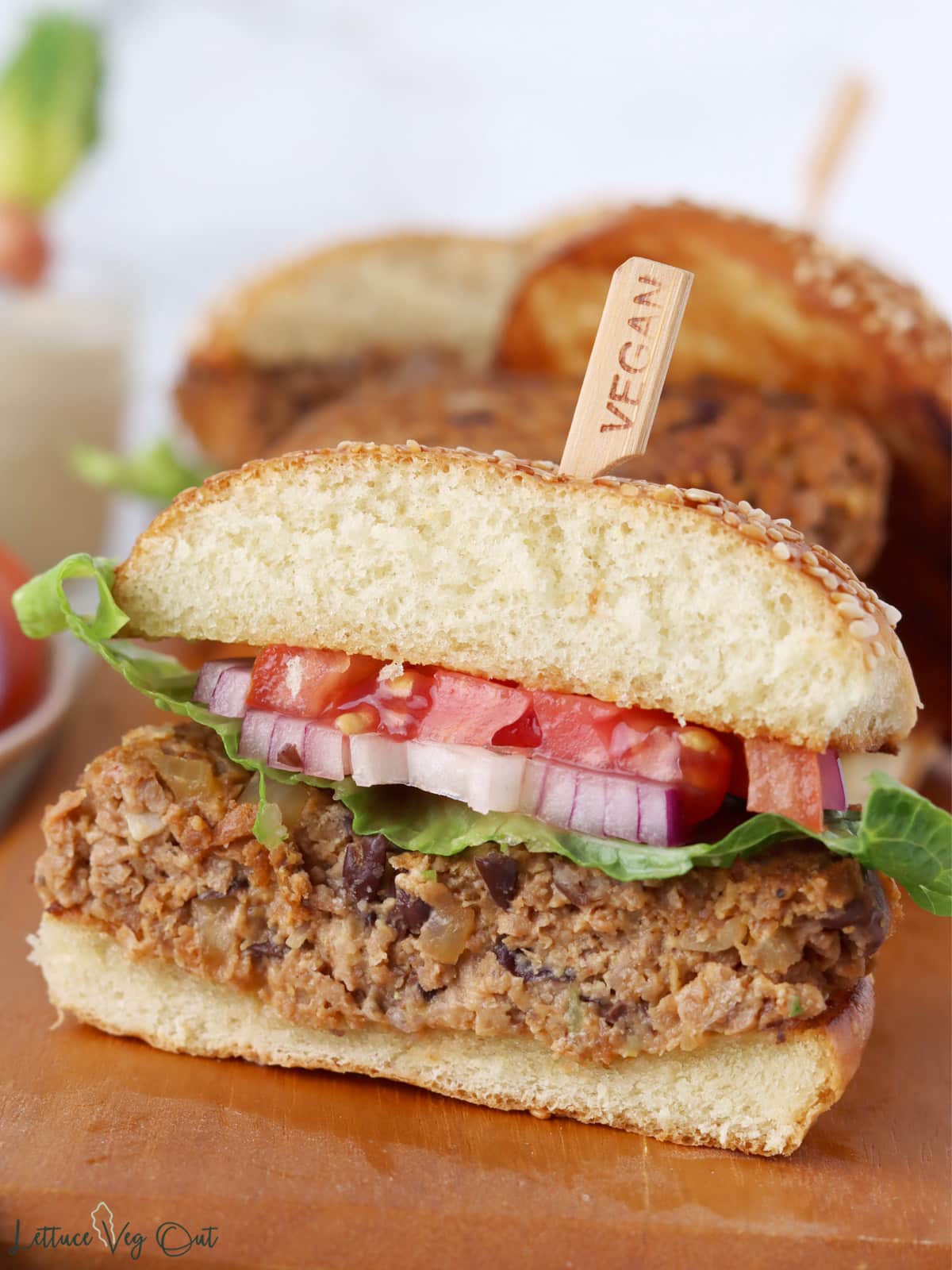 Soy protein burger cut in half to show inside, prepared on a sesame bun with tomato, lettuce and red onion.