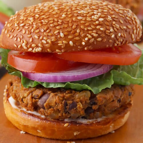 Close up of a TVP burger on a sesame bun with tomato, lettuce and red onion.
