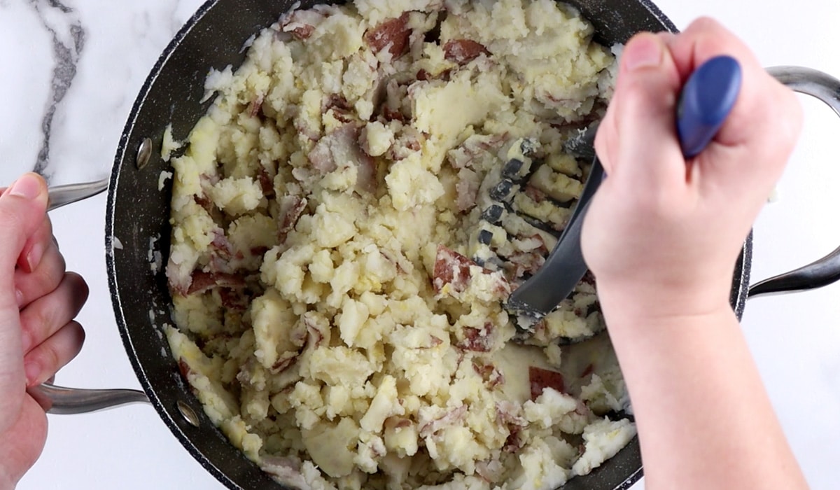 Hand mashing potatoes in a large pot.