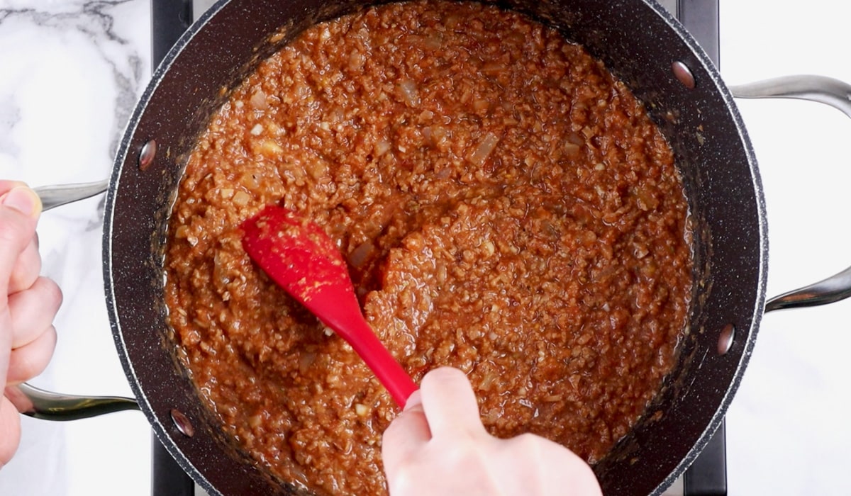 Hand stirring pot of simmering TVP spaghetti sauce.