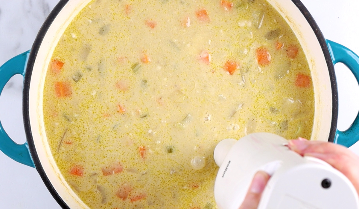 Immersion blender beginning to blend a large pot of potato soup.